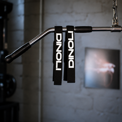 Black DINOLI auto-lock lifting straps with white branding hanging from a cable machine lat pulldown bar in a gym.