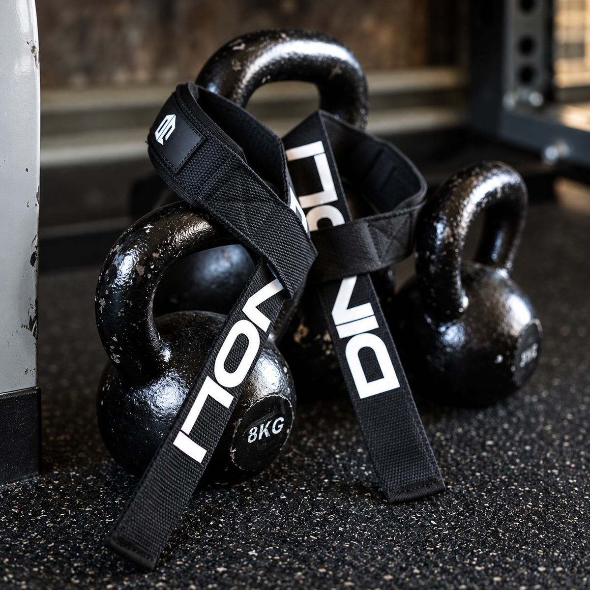 Black DINOLI auto-lock lifting straps with padded wrist supports draped over kettlebells on a gym floor.